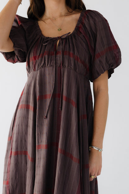 Close dress view of a young woman wearing a brown plaid dress with a full skirt, empire waist and balloon sleeves.