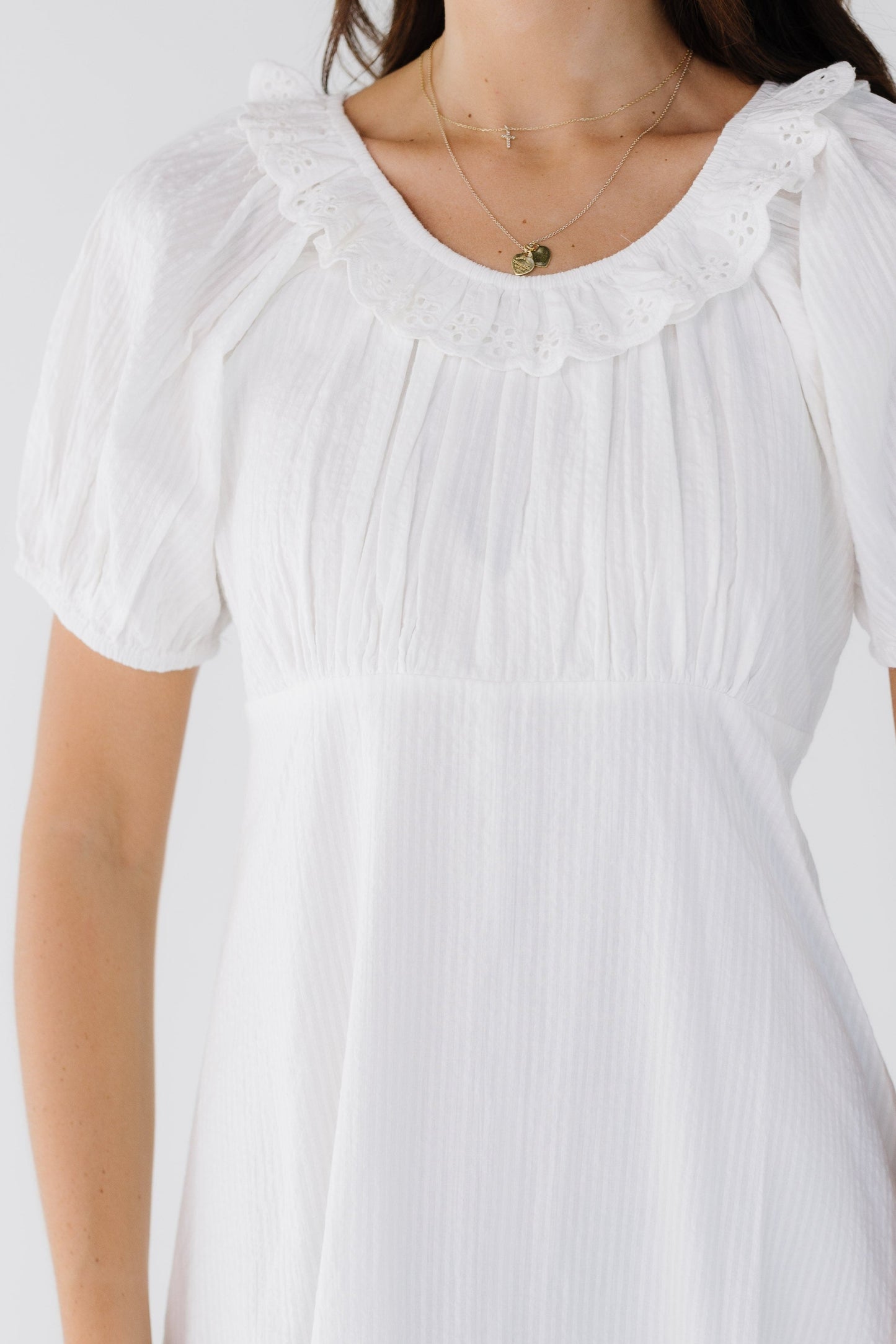 Close dress view of a woman wearing a white stripe dress with an empire waist, A-line skirt, scoop neckline with an eyelet ruffle and short puff sleeves.