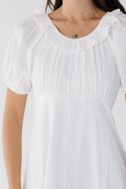 Close dress view of a woman wearing a white stripe dress with an empire waist, A-line skirt, scoop neckline with an eyelet ruffle and short puff sleeves.