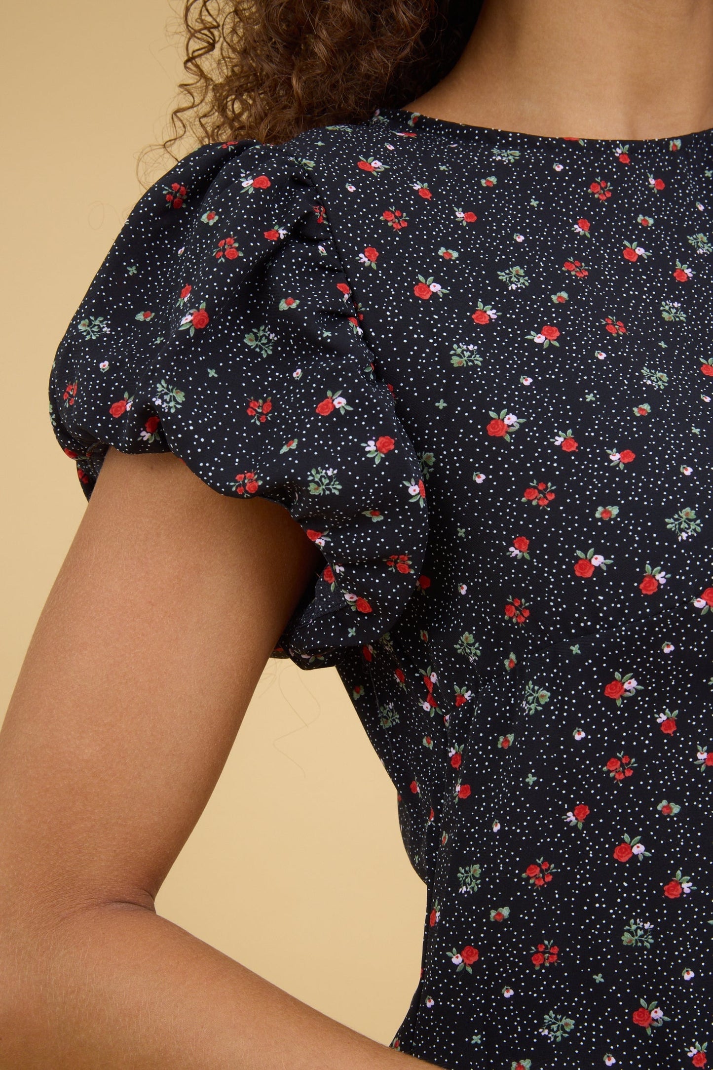 Close view of a teenage girl wearing a close fitting black floral dress with a round neckline and gathered cap sleeves.