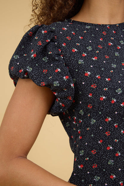 Close view of a teenage girl wearing a close fitting black floral dress with a round neckline and gathered cap sleeves.