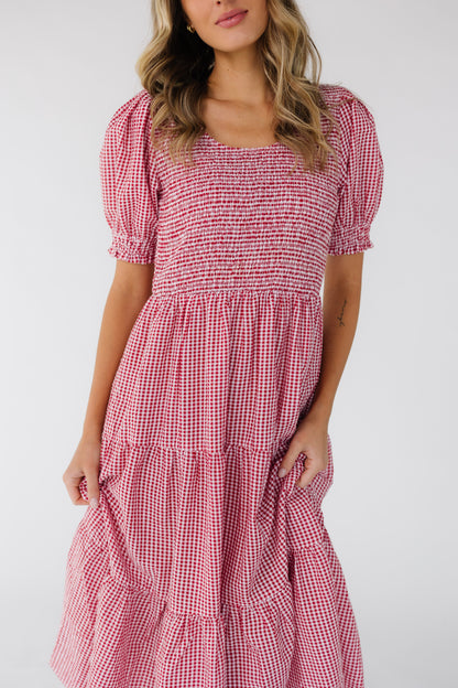 Closer vie of a woman wearing a gingham dress in red & white with multiple gathered tiers, a smocked bodice and short puff sleeves.