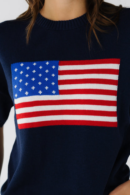 Close view of a woman wearing a navy short sleeve sweater with a large front American flag graphic.