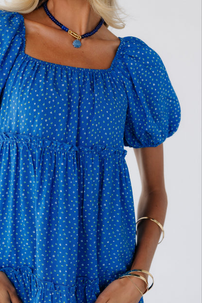 Close up view of a woman wearing a blue floral print midi dress with large puff sleeves and a square elastic neckline.
