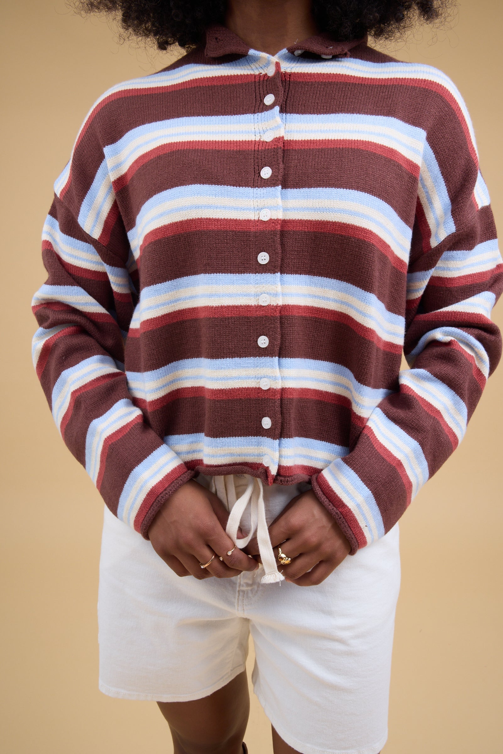 Close view of a woman wearing a brown multicolor & stripe button down cardigan with long sleeves.