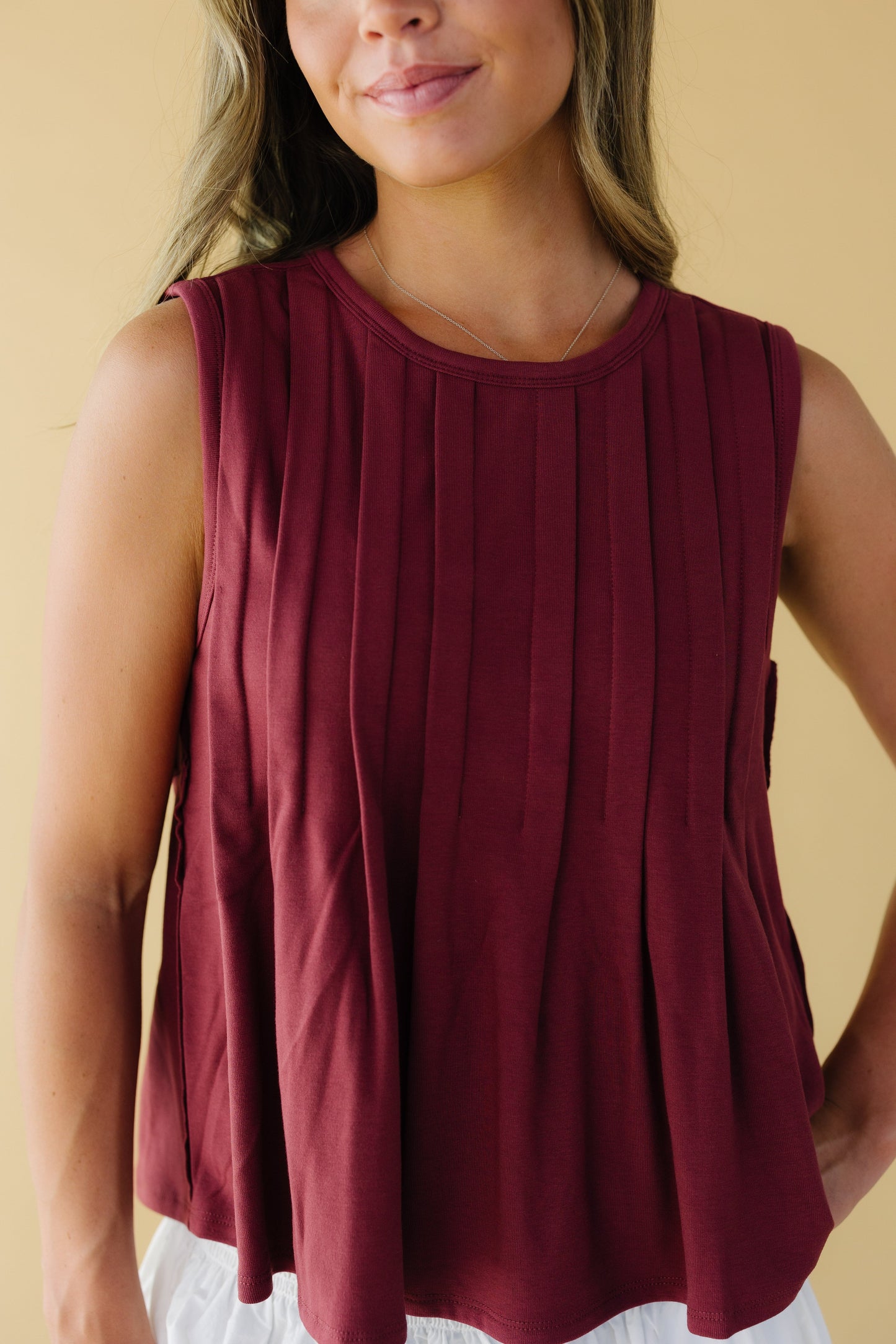 Close view of a wine color sleeveless blouse with a round neckline and front pleats.