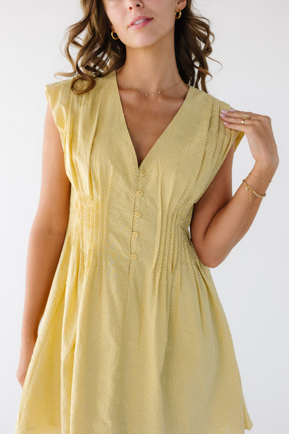 Woman wearing a yellow sleeveless short dress with waist pleats all around the waist.