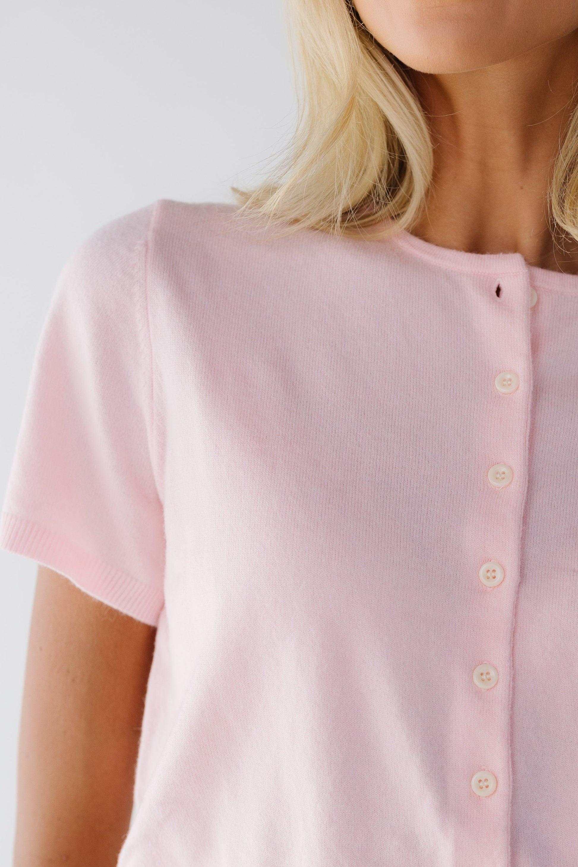 Close view of a young woman wearing a light pink cardigan with a round neckline and short sleeves.