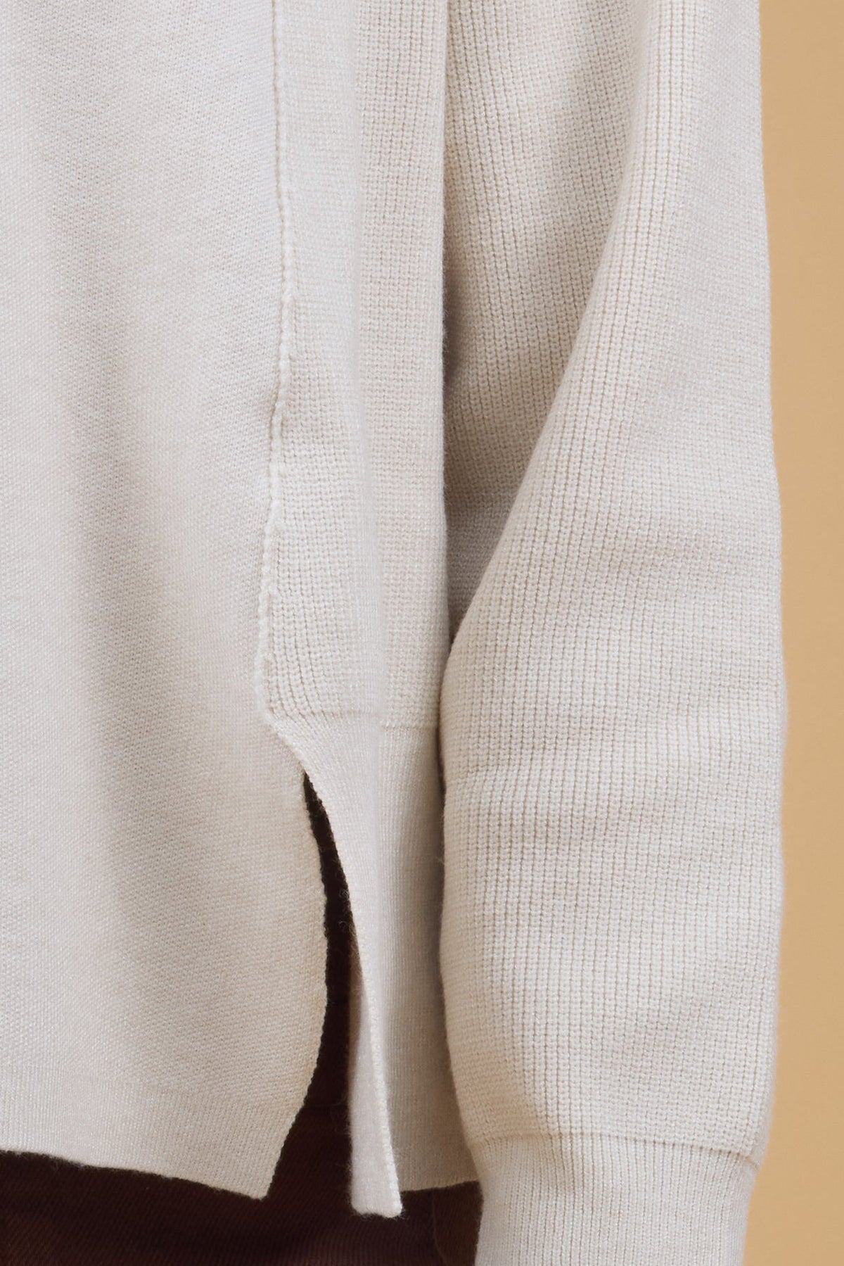 Close detail view of a woman wearing a knit top with ribbed side panel & sleeves with a smooth knit front panel.