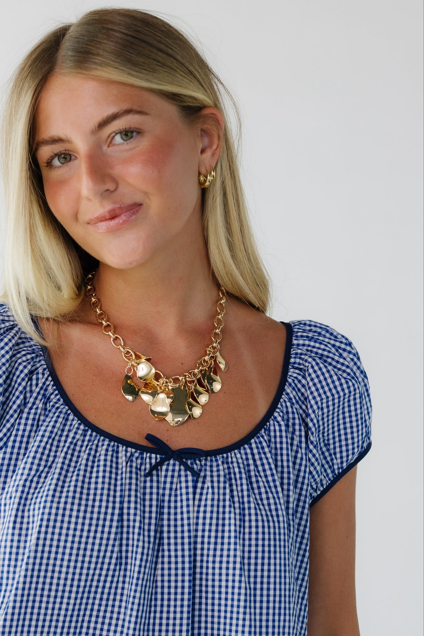 Close view of a woman wearing a navy & white gingham dress with short puff sleeves,  and a wide scoop neckline.