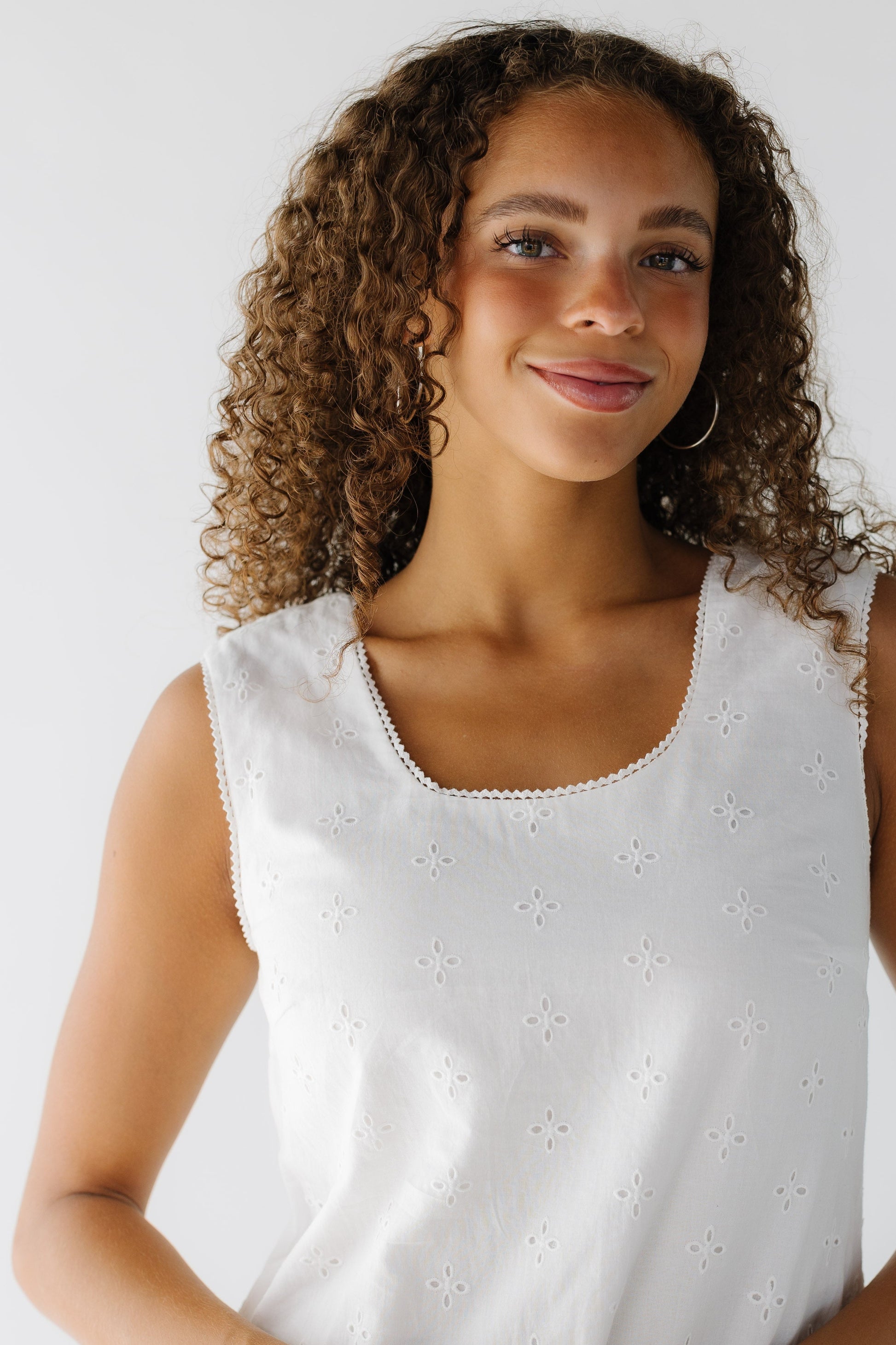 A close view of a teenage girl wearing a sleeveless white eyelet dress with a scoop neckline.