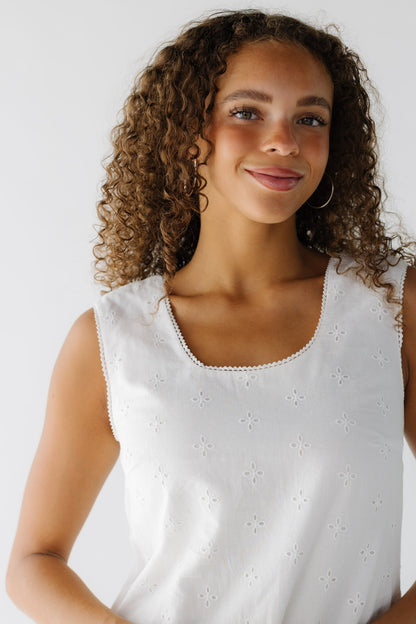 A close view of a teenage girl wearing a sleeveless white eyelet dress with a scoop neckline.