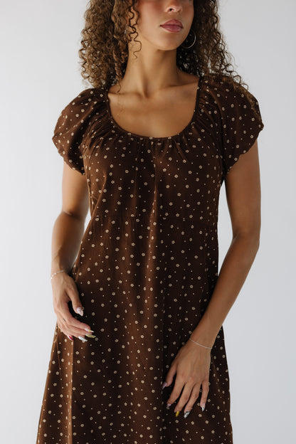Close view of a teenage girl wearing a brown floral dress with a gathered scoop neckline and short puff sleeves.
