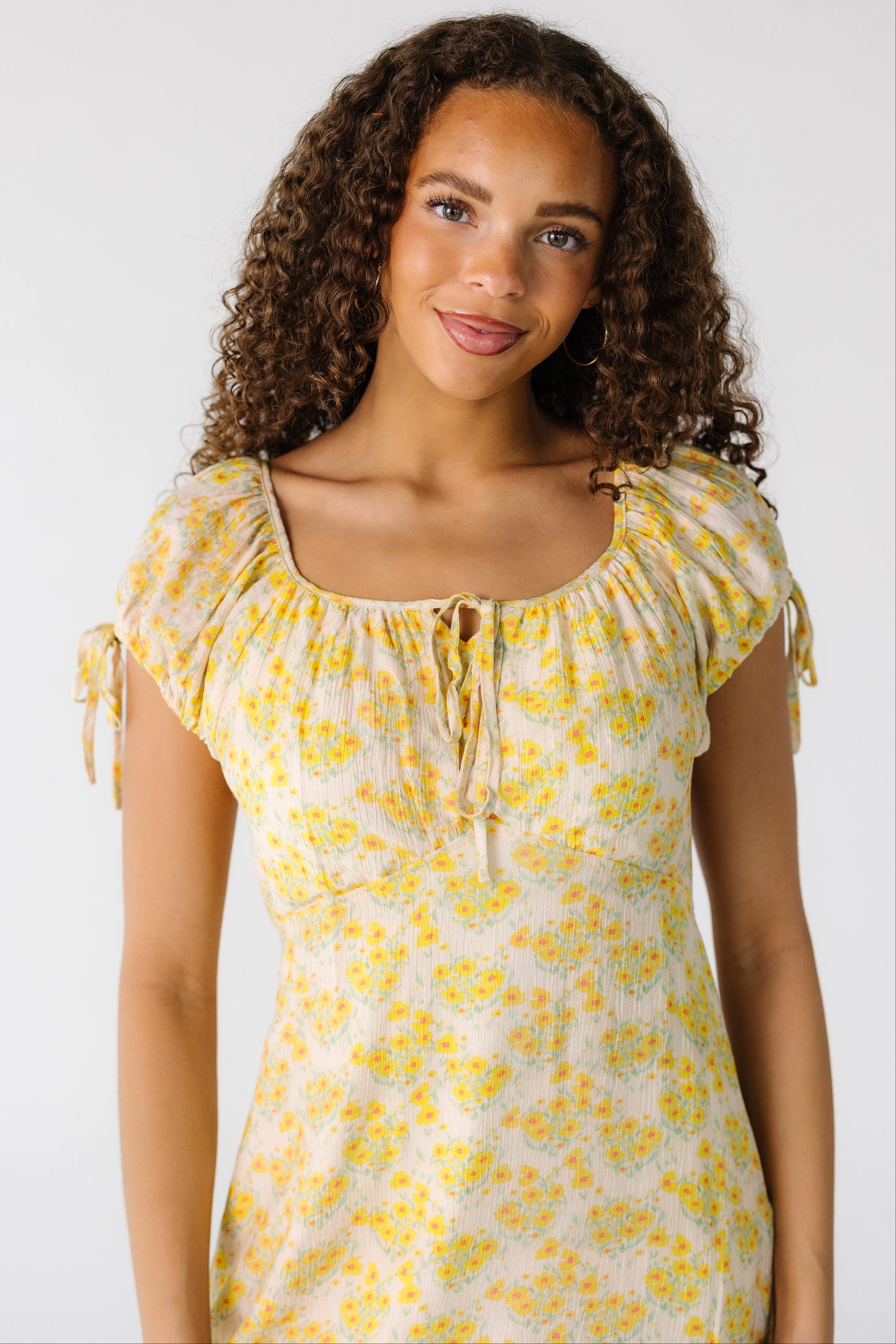 Teenage girl wearing a yellow floral print dress with a square neckline and short puff sleeves and a pointed empire dress.