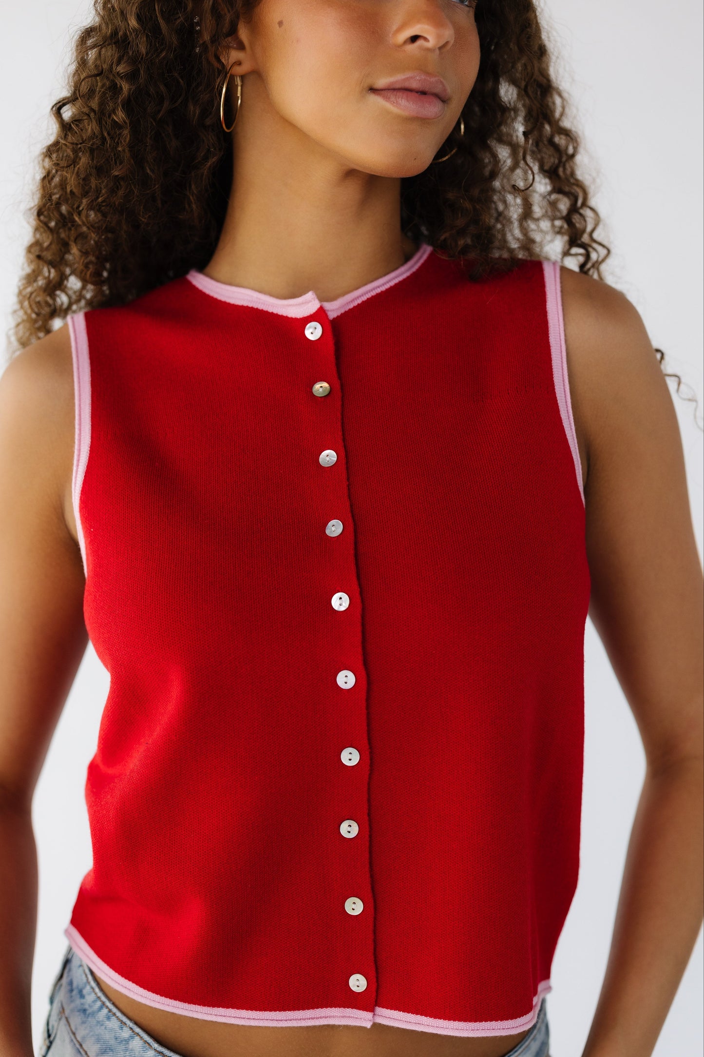 Close up view of a teen girl wearing a red knit button down top with pink hems.