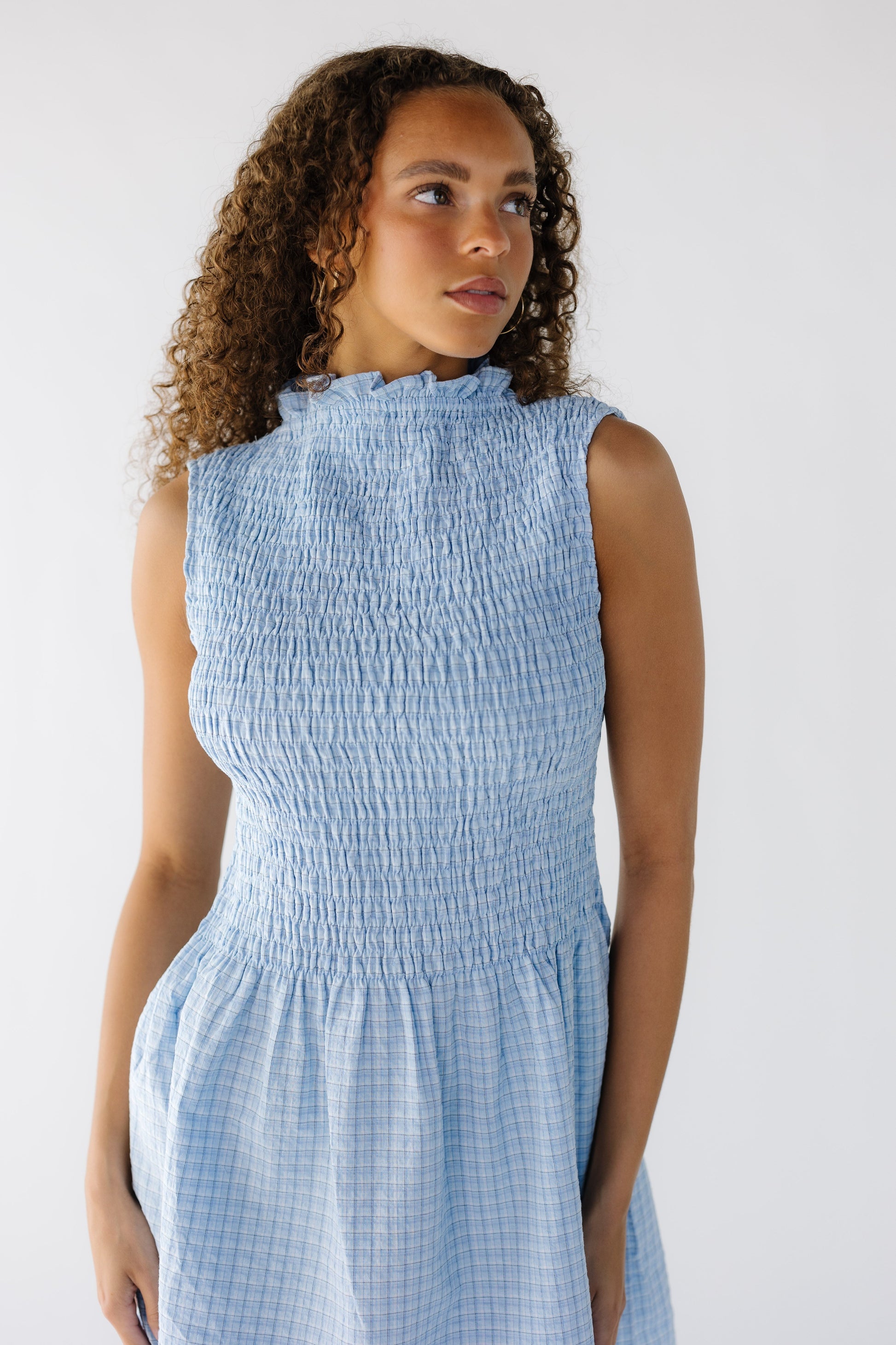 Close view of a teen girl wearing a blue plaid ,sleeveless short dress with a riffled neckline, smocked bodice.