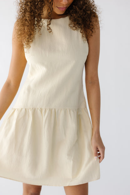 Closer view of a teenage girl earing a sleeveless yellow dress hemmed above the knee with a gathered skirt.