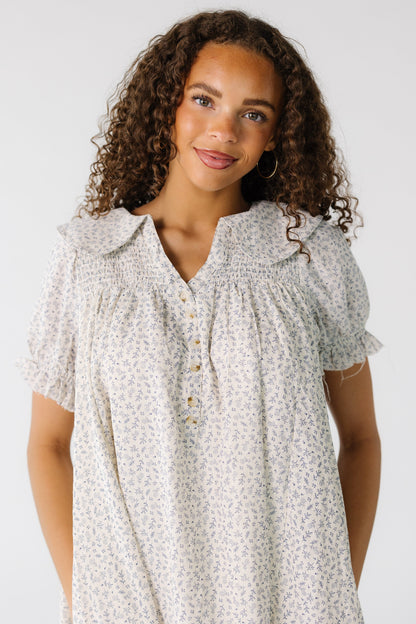 Teenage girl wearing a modest white and grey floral dress with a wide collar, V-neckline and short puff sleeves.