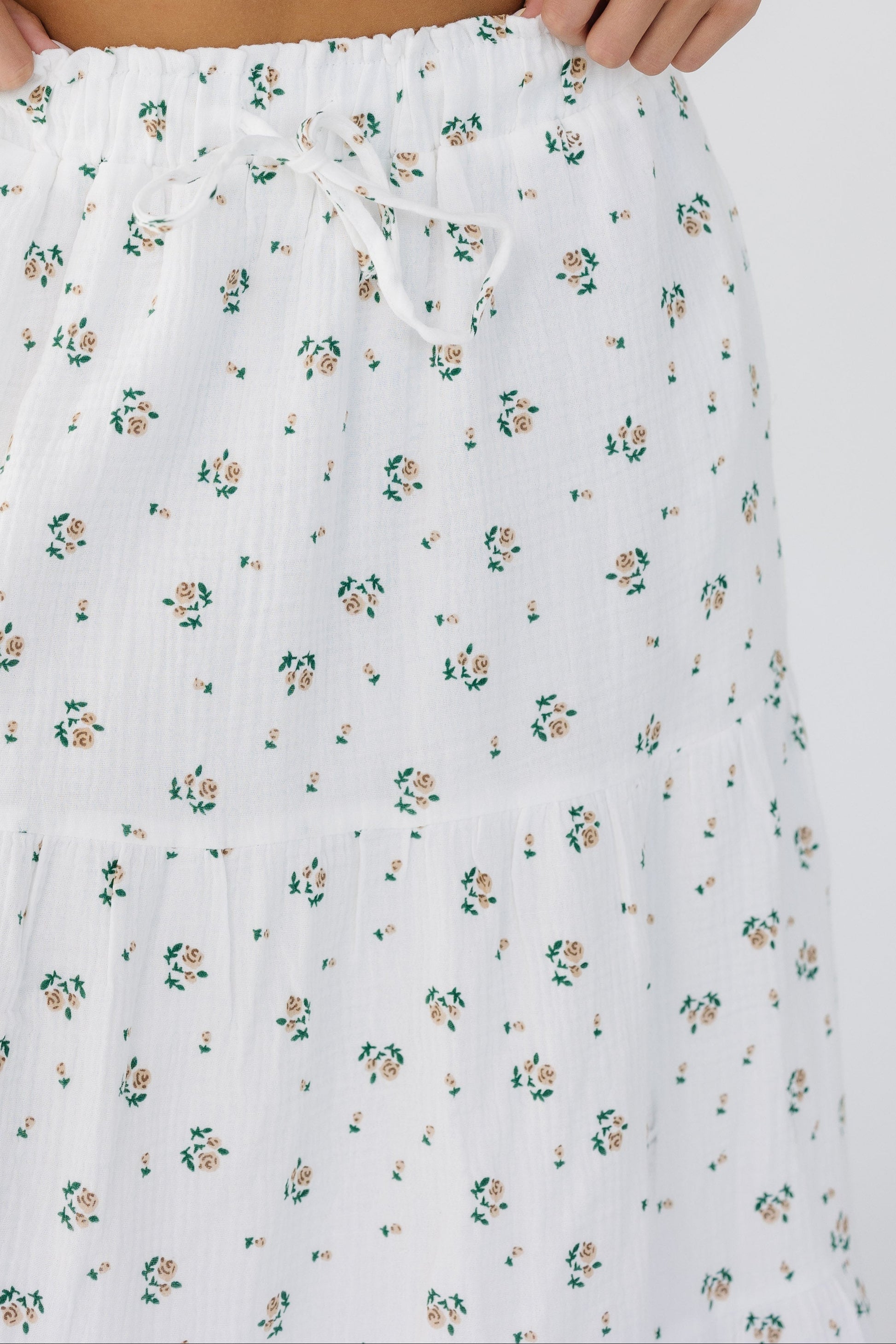 Close up view of a young woman wearing a white with pink floral print tiered skirt with an elastic waistband.
