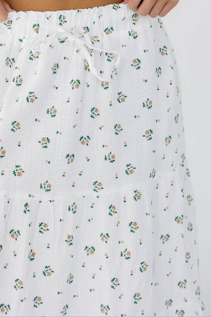 Close up view of a young woman wearing a white with pink floral print tiered skirt with an elastic waistband.