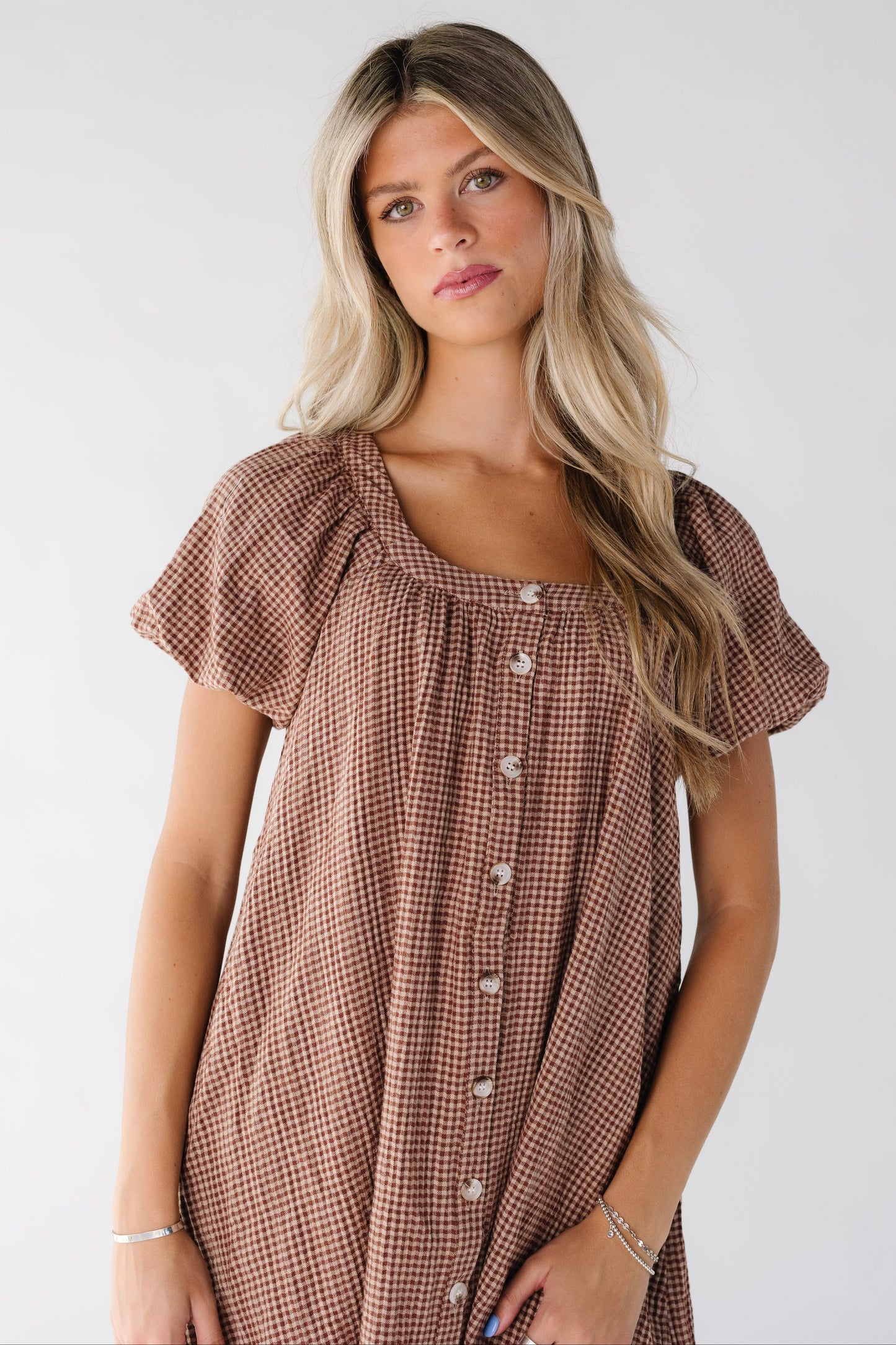 Close view of a woman wearing a brown gingham dress with a scoop neckline