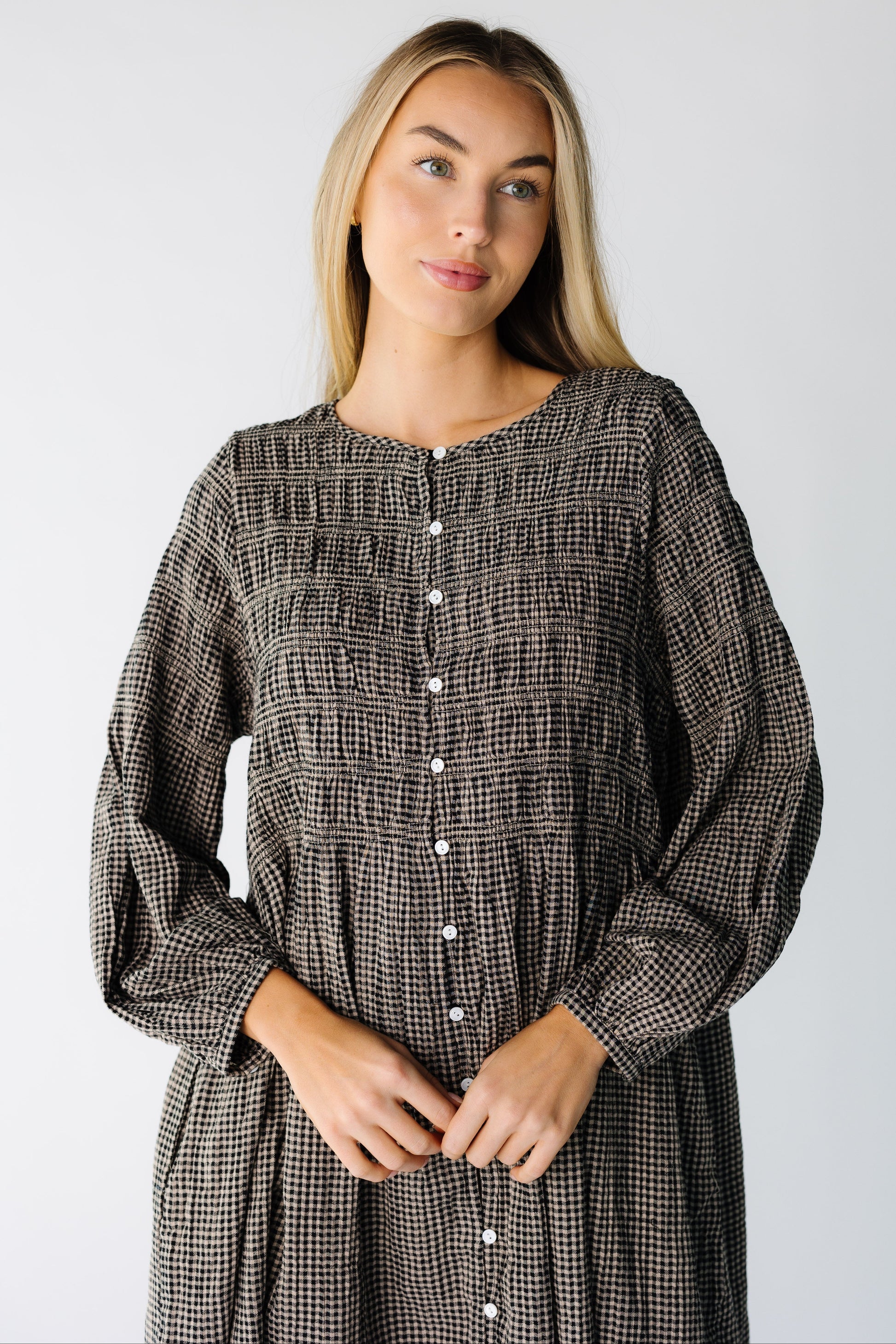 Close view of a woman wearing a black gingham button down dress with a round neckline and long sleeves