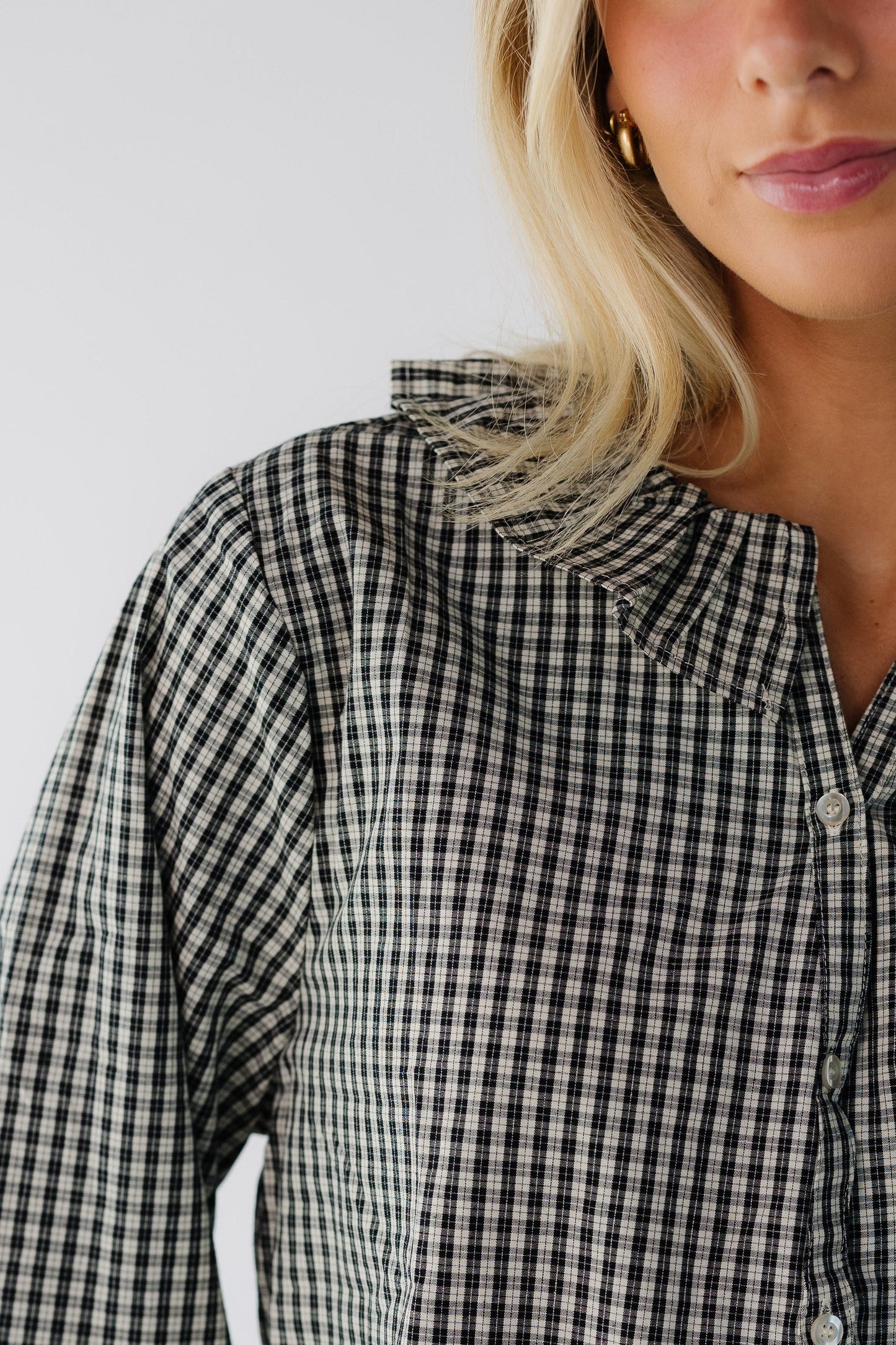 Close view of a young woman wearing a black plaid button down blouse ad a rufled collar.