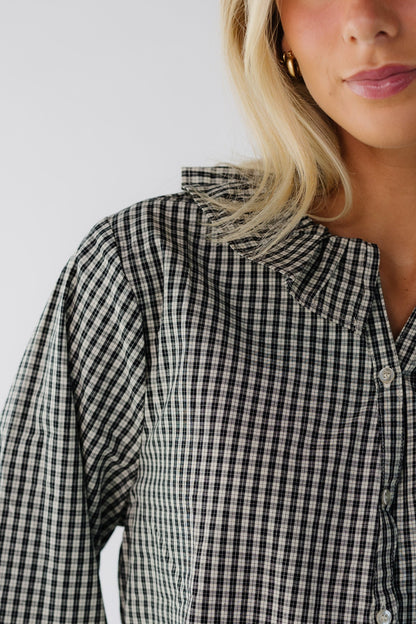 Close view of a young woman wearing a black plaid button down blouse ad a rufled collar.