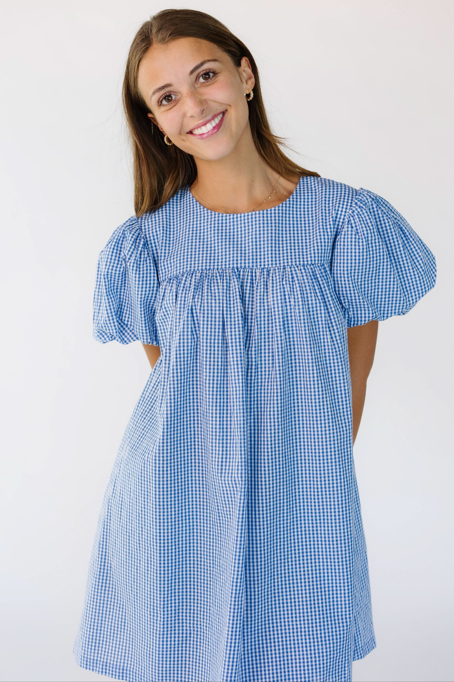 Young woman wearing a blue and white gingham short dress with large puff sleeves.