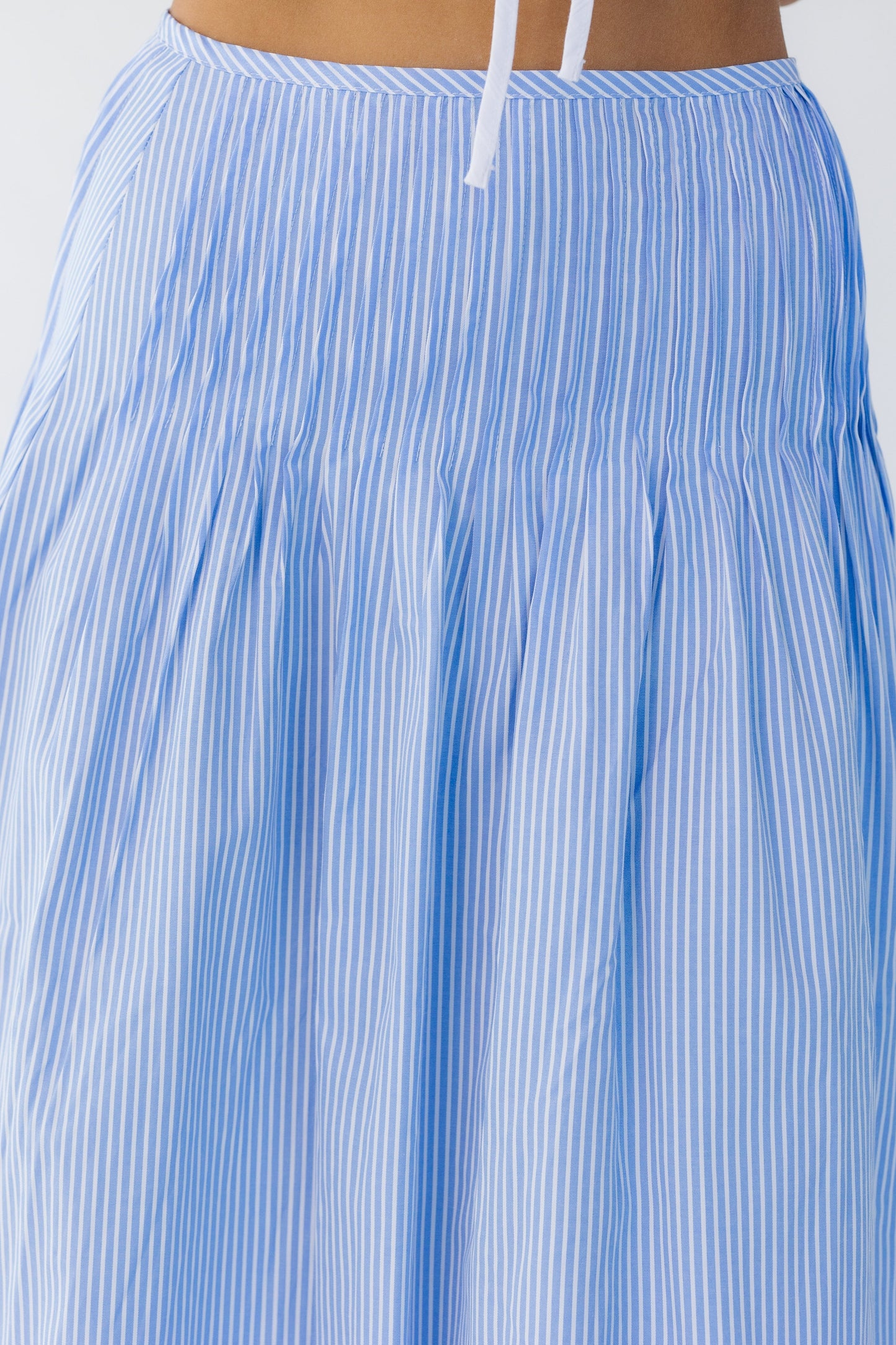 Close view of a young woman wearing a blue and white  stripe midi skirt with sewn down pleats.