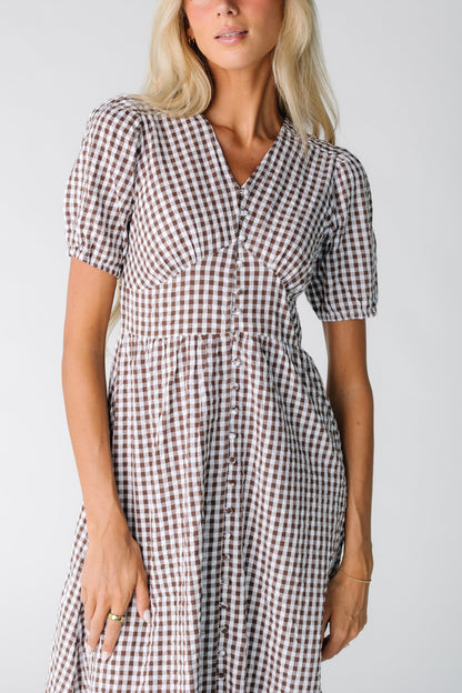 Close view of a woman wearing a button down brown and white gingham dress with snug waistband