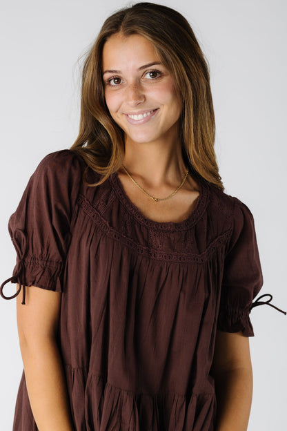 Close view of a woman wearing a brown dress with a scoop neckline and eyelet lace details