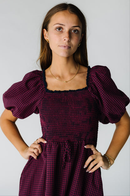 Close view of a woman wearing a burgundy gingham dress with a smocked bodice and square neckline