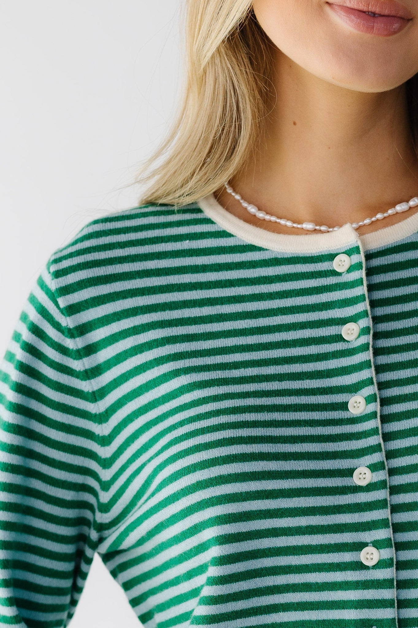 Close view of a woman wearing a green & light blue stripe cardigan with contrasting white neckline & buttons.