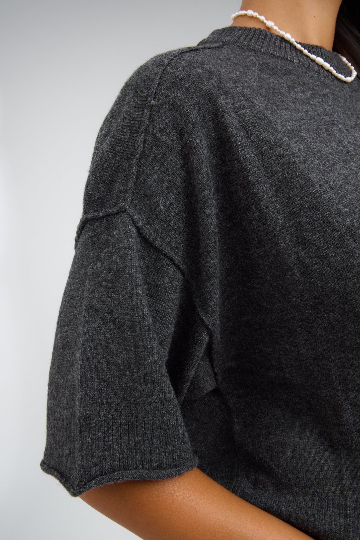 Close view of a woman wearing a charcoal lightweight sweater with exposed seams and rolled cuffs.