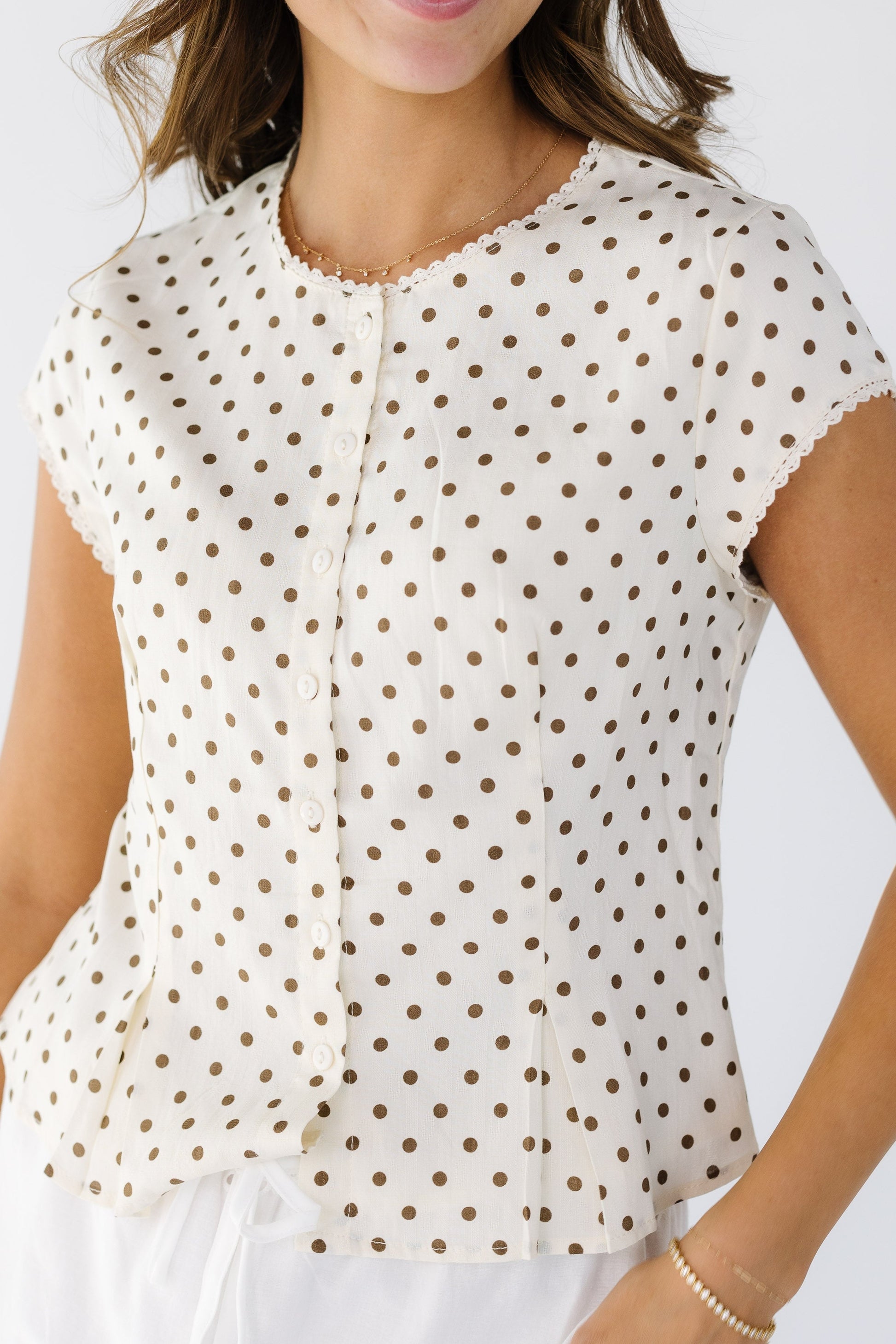 Closer view of a dressy cream and brown polka dot, button down top with lace trims.