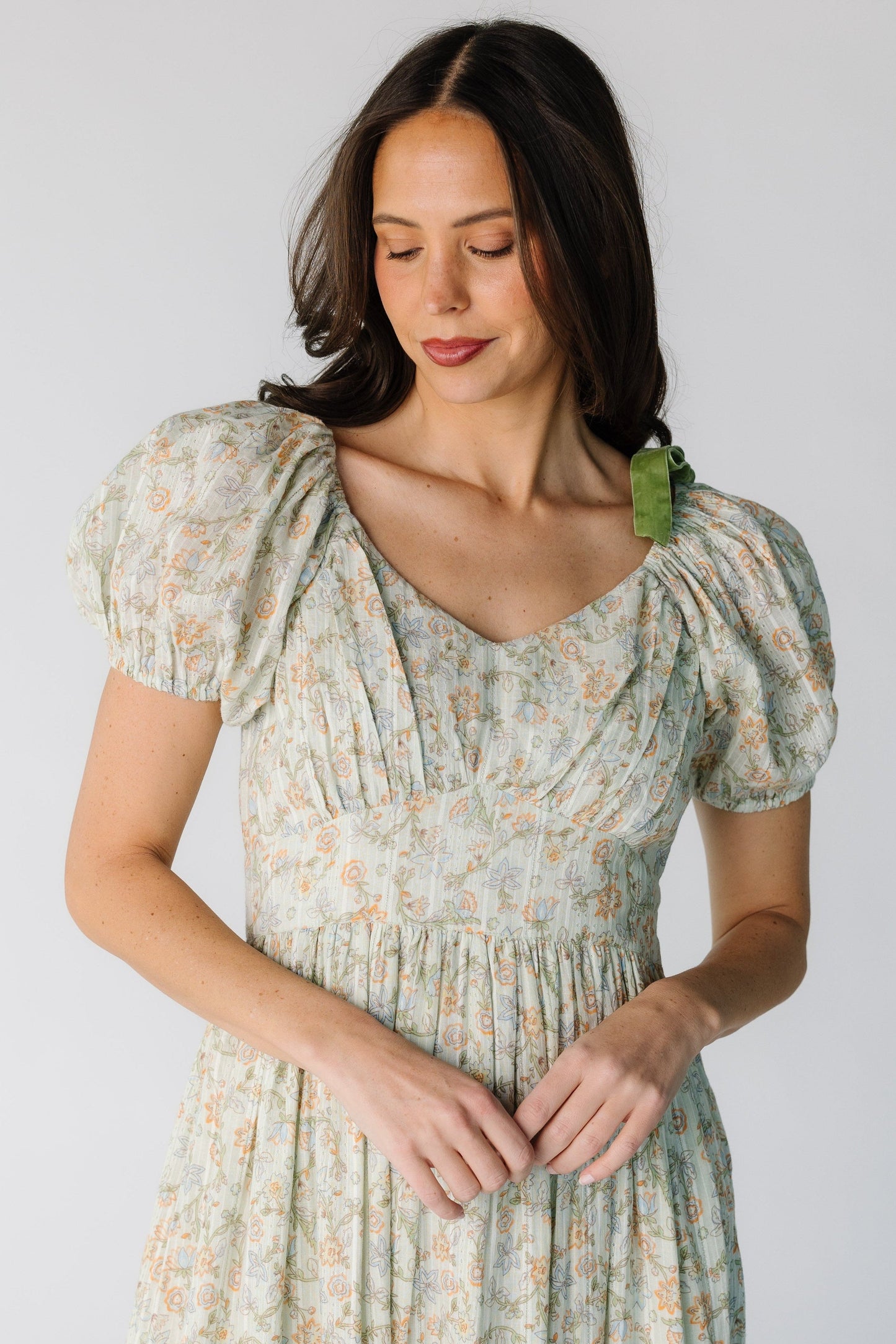 Close view of a woman wearing a green floral print dress with a wide pointed waistband, Sweetheart neckline, and short puff sleeves.