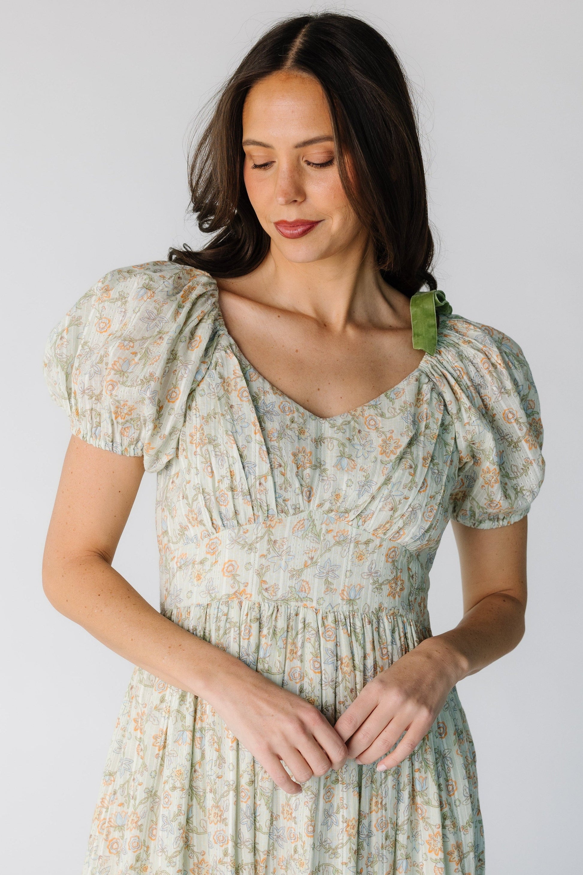 Close view of a woman wearing a green floral print dress with a wide pointed waistband, Sweetheart neckline, and short puff sleeves.