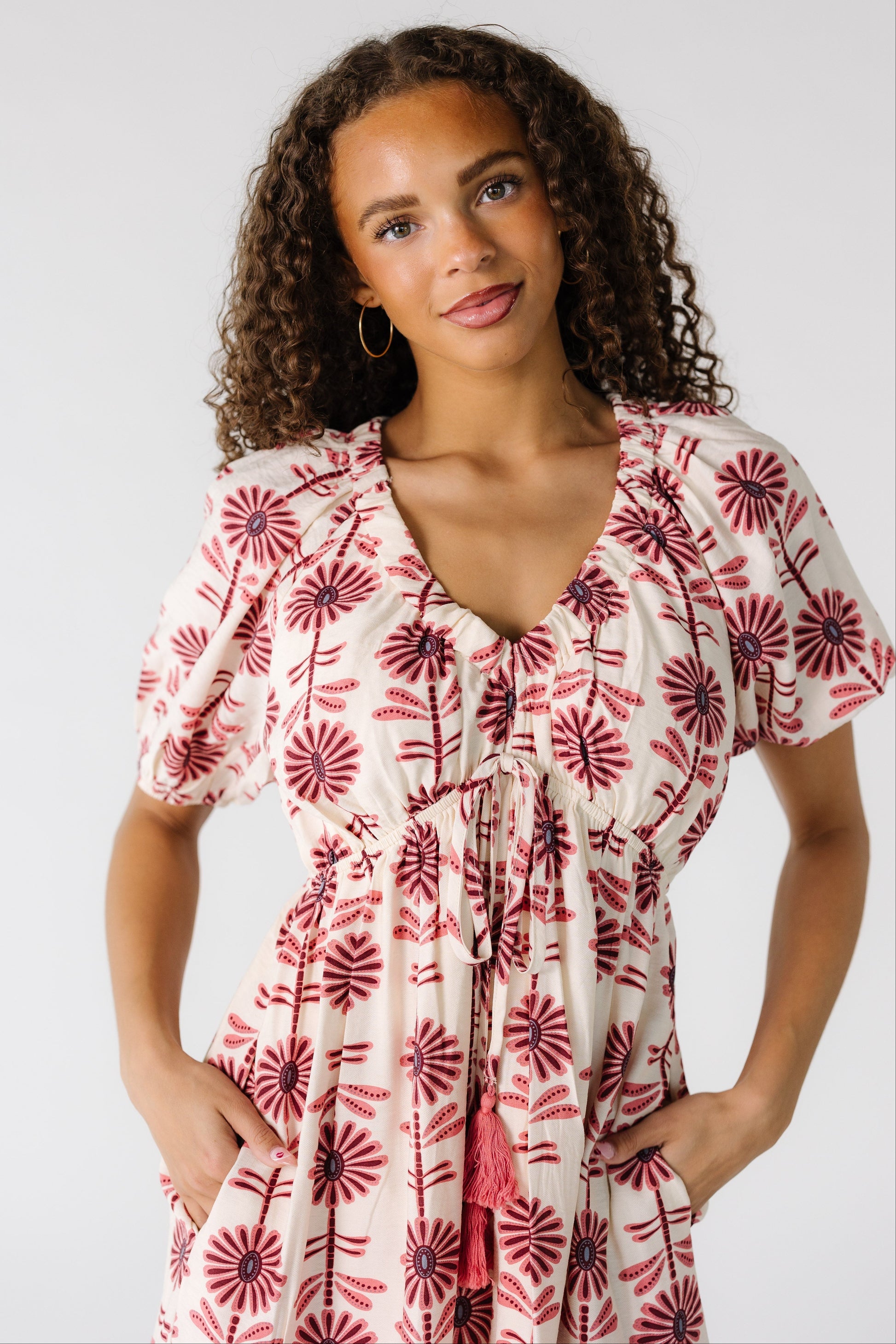 Close vie of a teenage girl wearing a cream dress with pink and mauve floral print with a V-neckline, short sleeves and a pointed empire waist.