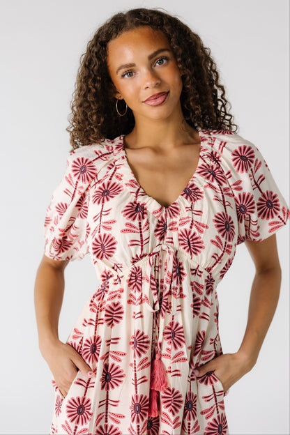 Close vie of a teenage girl wearing a cream dress with pink and mauve floral print with a V-neckline, short sleeves and a pointed empire waist.