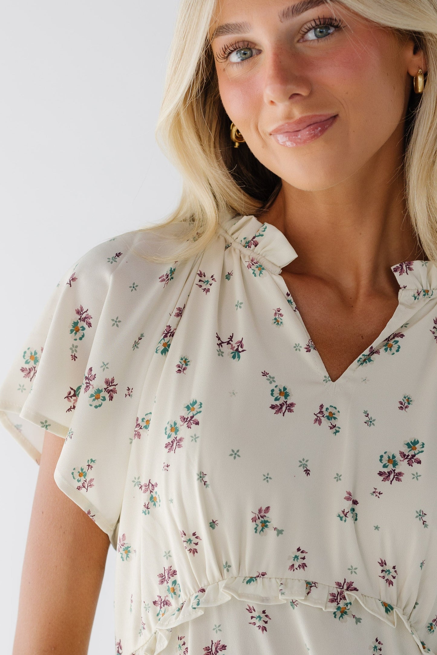 Close view of a woman wearing cream floral dress with short sleeves a V-neckline and a ruffled empire waist.