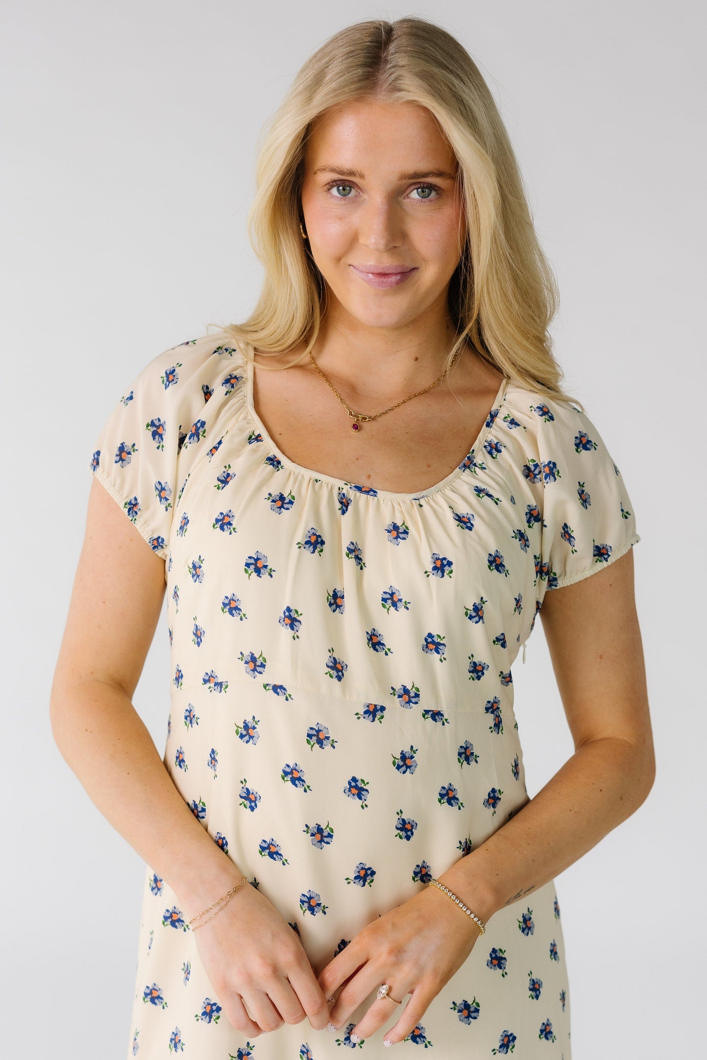 Close view of a woman wearing a cream dress with blue floral print and a Scoop neckline and short puff sleeves.