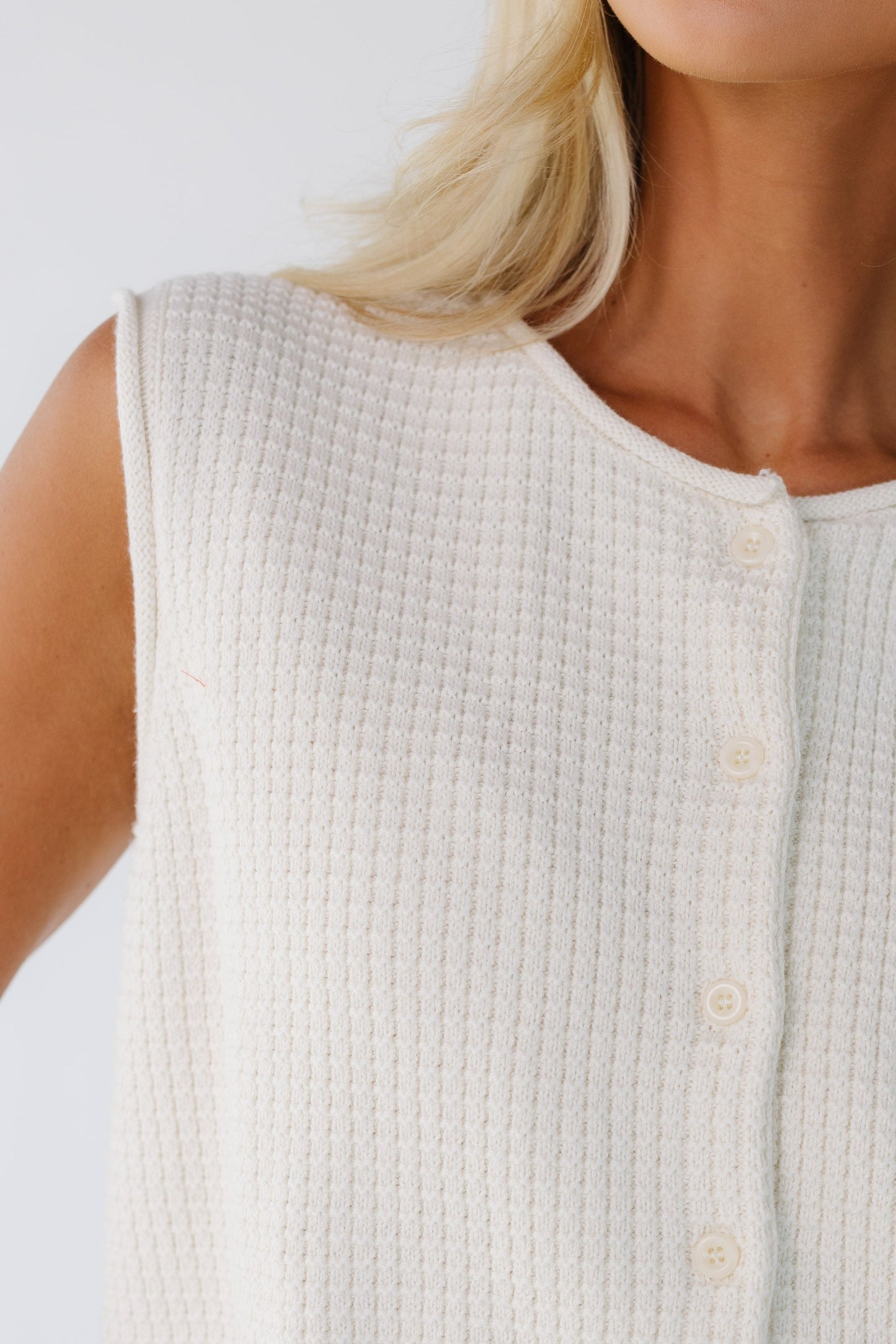 Close view of a woman wearing a textured sleeveless button down sweater vest with a rolled neckline and rolled armholes.