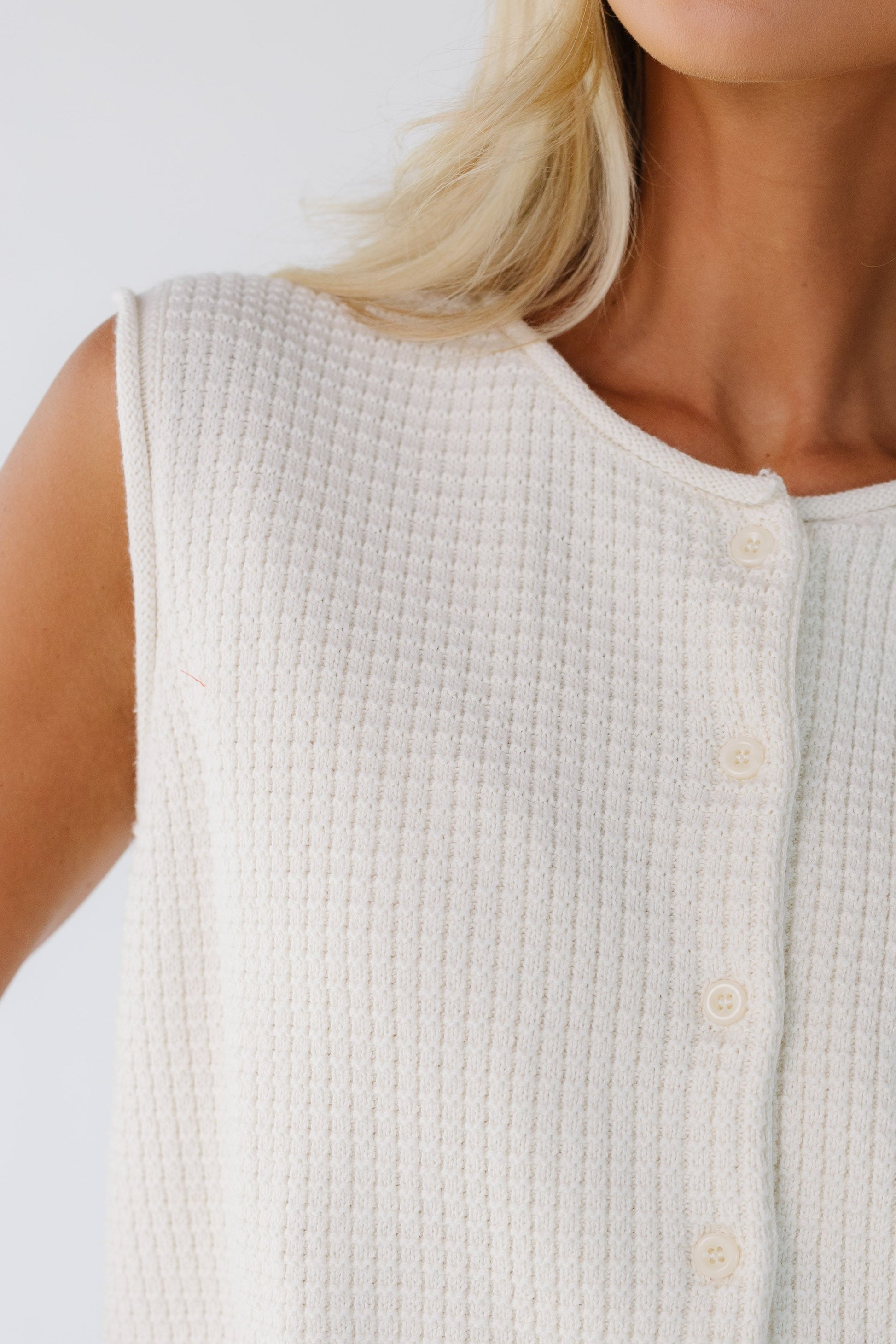 Close view of a woman wearing a textured sleeveless button down sweater vest with a rolled neckline and rolled armholes.