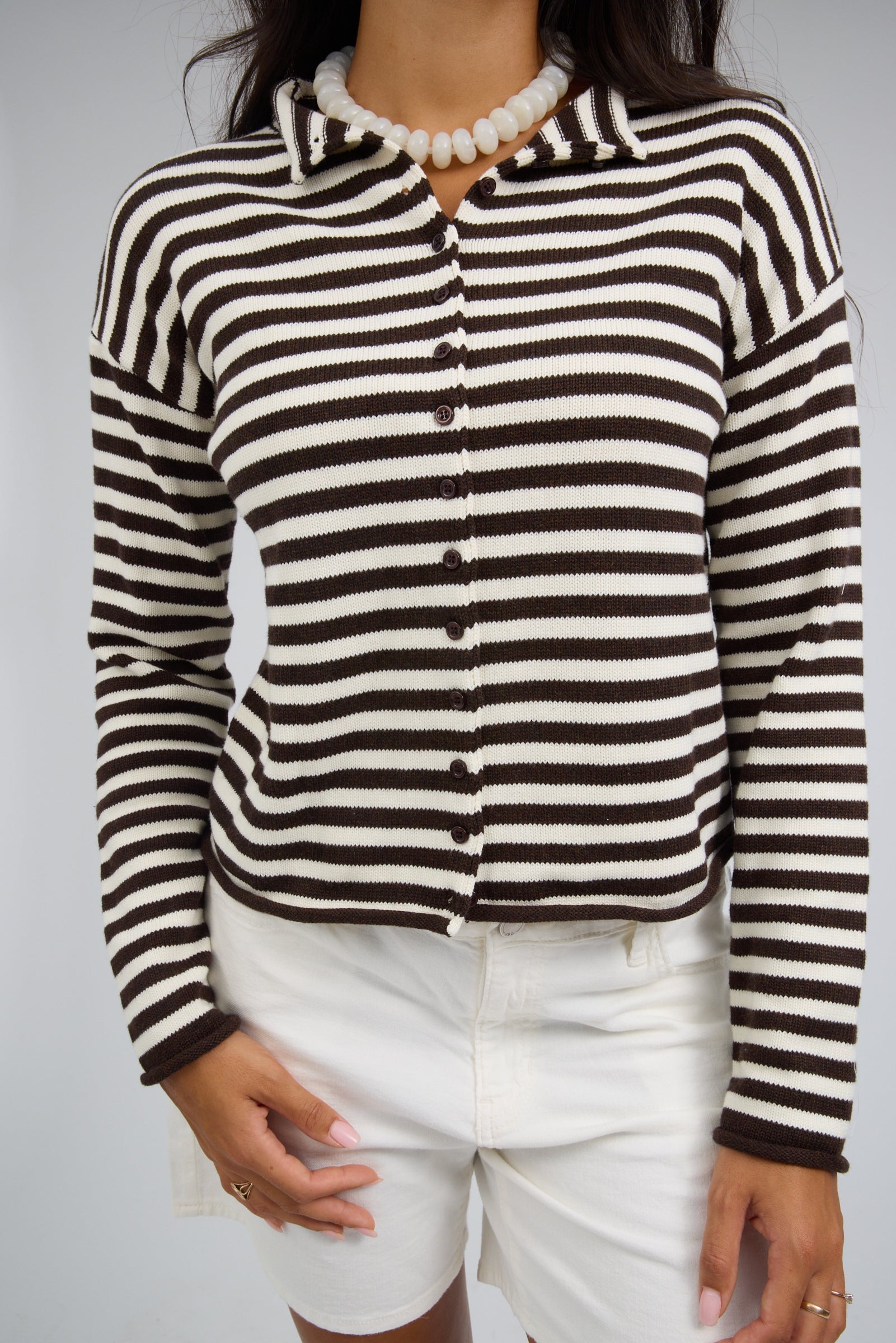 Close view of a woman wearing a brown & white stripe  button down cardigan with long sleeves and rolled cuffs.