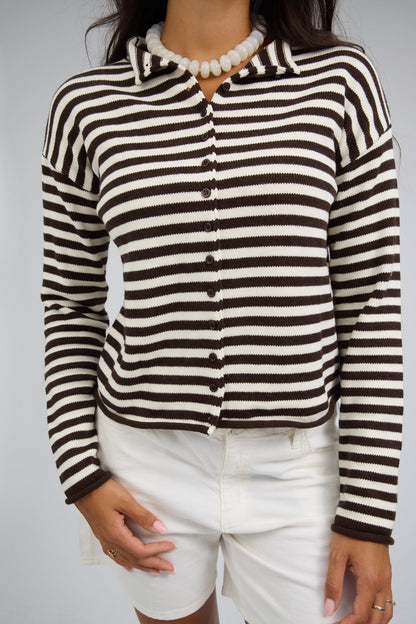 Close view of a woman wearing a brown & white stripe  button down cardigan with long sleeves and rolled cuffs.