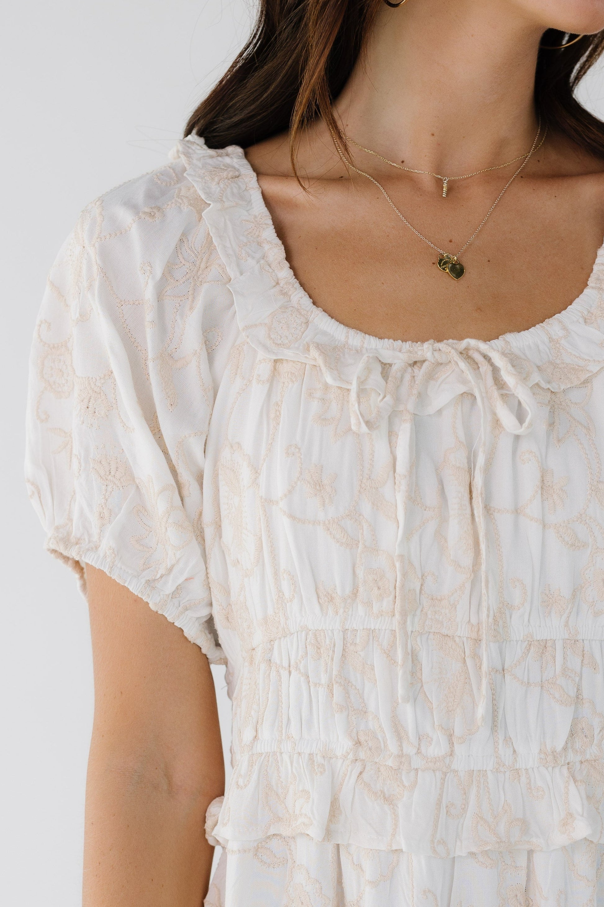 Closer view of a young woman wearing a white embroidered dress with a ruffled neckline and a wide waist.