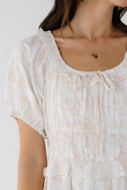 Closer view of a young woman wearing a white embroidered dress with a ruffled neckline and a wide waist.