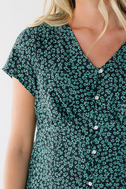 Close view of a woman wearing a button down green floral dress with a V-neckline, short sleeves and an empire waist.