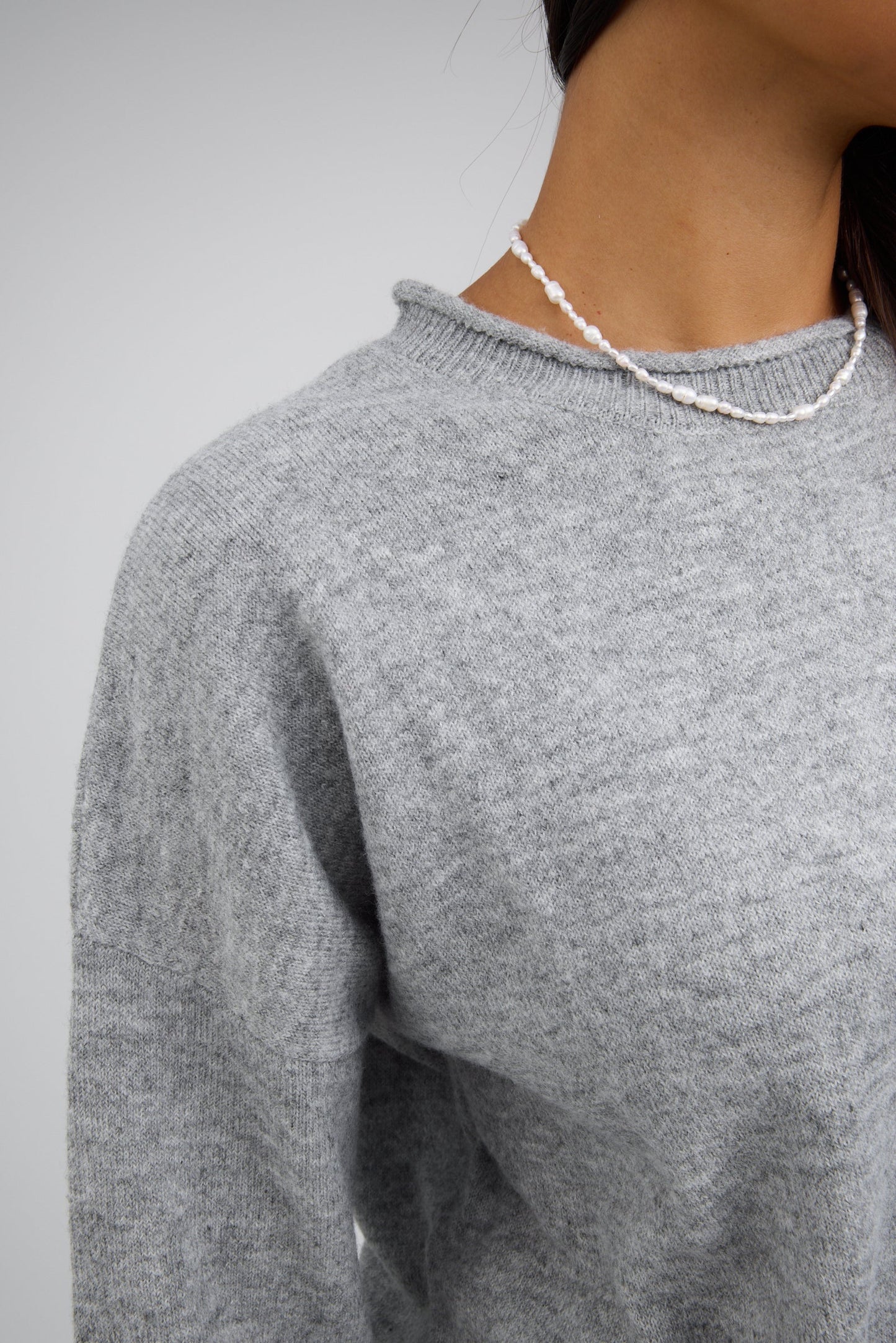 Close view of a woman wearing a grey pullover sweater with a ribbed and rolled neckline.